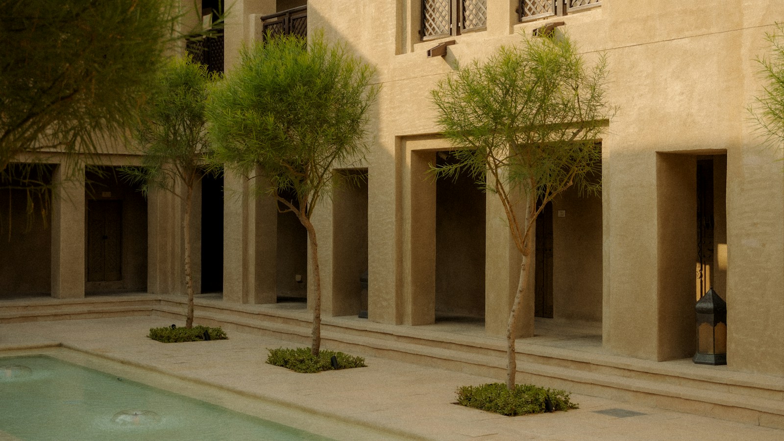 Sunlit stone courtyard surrounding a still pool and leafy trees
